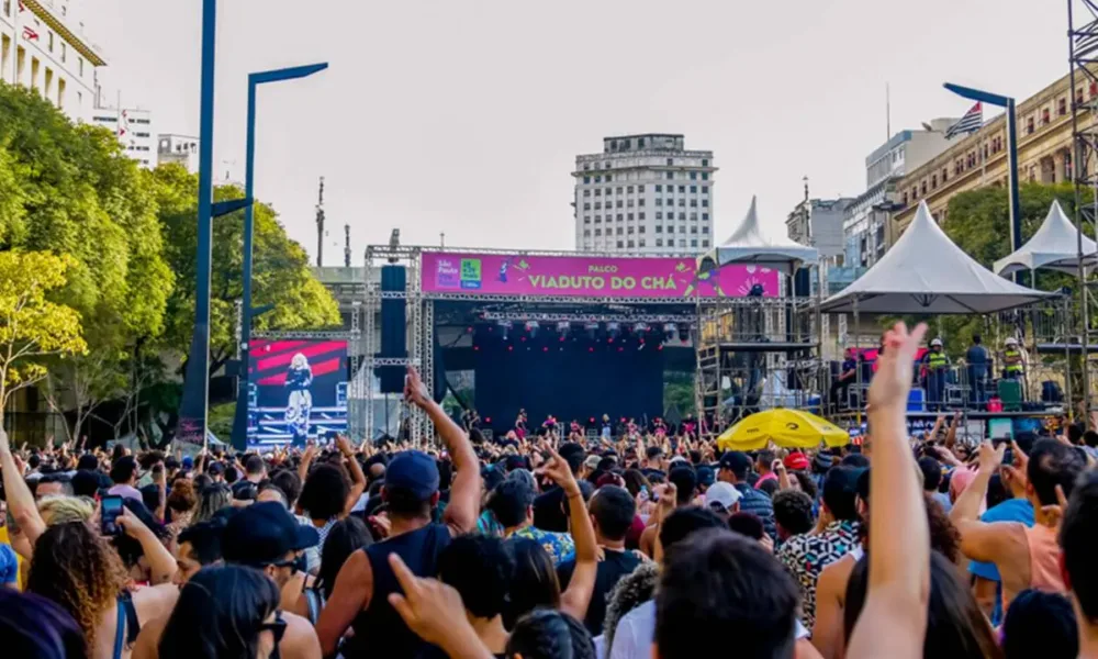 Vista do público de palco do Viaduto do Chá durante virada cultural de São Paulo. Está de dia e show está cheio.