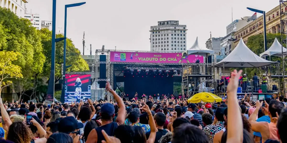 Virada Cultural 2026 | São Paulo Para, Ouve e Dança por 24 Horas Seguidas Vista do público de palco do Viaduto do Chá durante virada cultural de São Paulo. Está de dia e show está cheio.