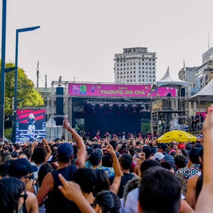 Vista do público de palco do Viaduto do Chá durante virada cultural de São Paulo. Está de dia e show está cheio.