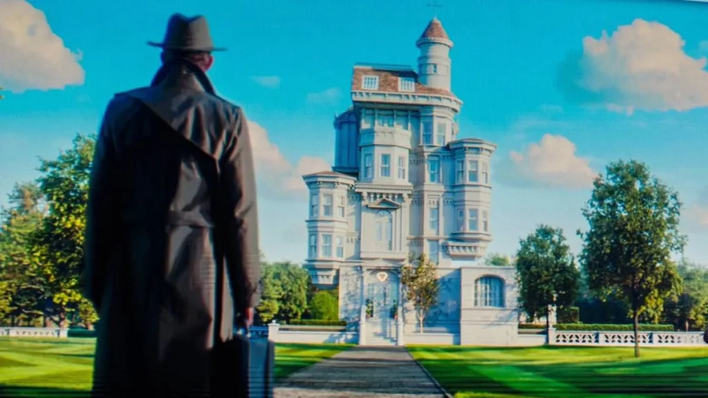 VisionQuest | Novo Trailer Apresenta Jocasta e Poderes de Tommy 1 Visão, de sobretudo, de costas, em ambiente em estética "glitch" frente a uma casa em ambiente verde de cores vivas, céu azul. Ele carrega uma mala na mão direita. VisionQuest