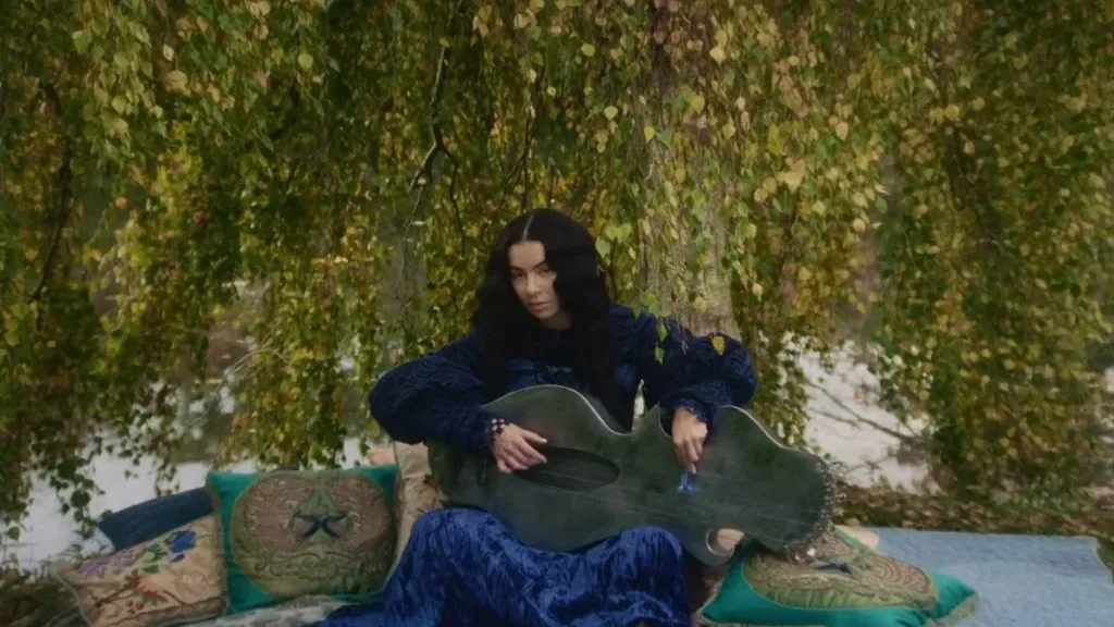 Esta imagem mostra a cantora Charli XCX tocando uma harpa escultural criada pela artista Amanda Camenisch no filme "100 Nights of Hero".