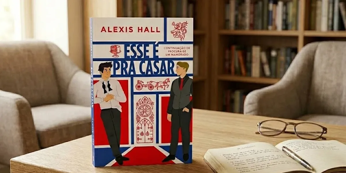 Esse é Pra Casar | O Amor Continua Complicado — E Deliciosamente Divertido O livro na imagem é "Esse é pra casar", de Alexis Hall, de pé em um ambiente confortável de leitura, com uma estante ao fundo, luz ambiente diurna. Há um livro com anotações e caneta, e um óculos fechado na mesma mesa.