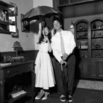 Ariana Grande e Justin Long em foto debaixo de guarda chuva em ambiente interno, temática dos anos 50, preto e branco, para o clipe de "Hate That I Made You Love Me".