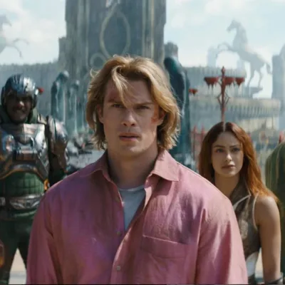 Esta é uma cena do filme live-action Mestres do Universo, com estreia prevista para junho de 2026. Adam está ao centro, camisa rosa, e o elenco de Eternia ao fundo.