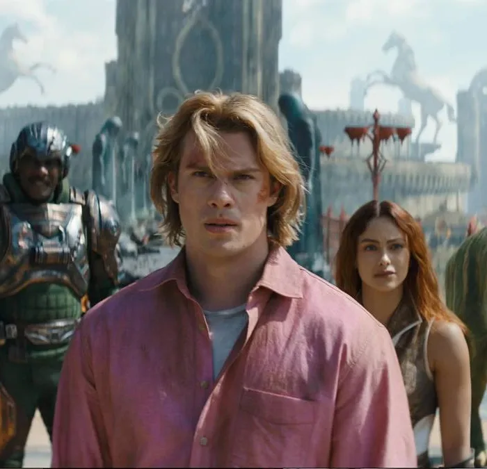 Esta é uma cena do filme live-action Mestres do Universo, com estreia prevista para junho de 2026. Adam está ao centro, camisa rosa, e o elenco de Eternia ao fundo.