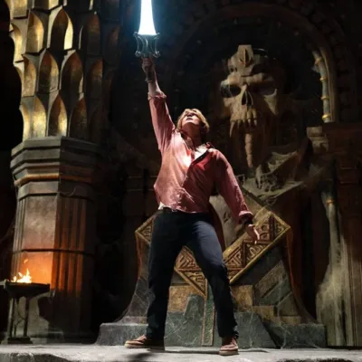 Esta é uma cena do filme live-action Mestres do Universo, estrelado por Nicholas Galitzine. A imagem mostra o protagonista em uma pose clássica, erguendo a Espada do Poder.