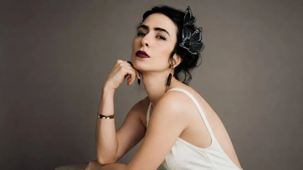 Marisa Monte, vestido branco, posando com mão sobre queixo, fundo cinza ao fundo. Imagem gerada por IA.