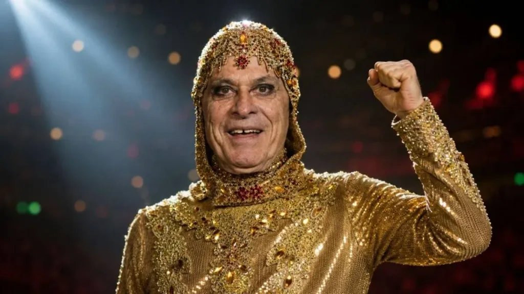 Ney Matogrosso com punho esquerdo erguido, sorrindo, vestindo roupa dourada de brilhantes. Imagem gerada por IA.