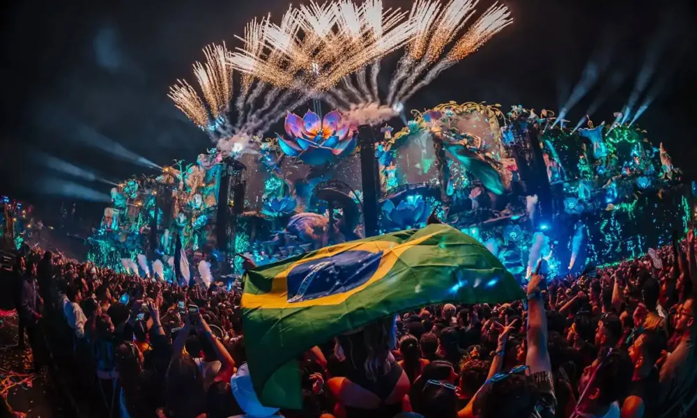 Aeromovie do Tomorrowland 2025, imagem promocional com palco iluminado à noite. Pessoa carrega bandeira do Brasil tremulando.