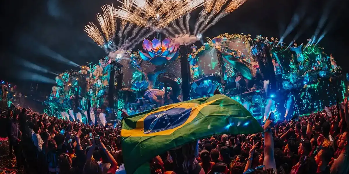 Aeromovie do Tomorrowland 2025, imagem promocional com palco iluminado à noite. Pessoa carrega bandeira do Brasil tremulando.