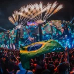 Aeromovie do Tomorrowland 2025, imagem promocional com palco iluminado à noite. Pessoa carrega bandeira do Brasil tremulando.
