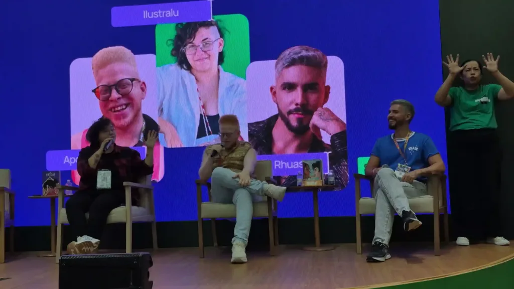 Nordeste Ficção | Novas Vozes Desafiam Estereótipos e Ampliam o Imaginário Sobre a Região na Bienal do Livro SP 1 Ilustralu, Pedro Rhuas e Apolo Andrade, apresentador e mediador, participam de uma conversa sobre literatura e ficção nordestina no Skeelo Talks, realizado durante a Bienal do Livro de São Paulo 2026. Os convidados estão sentados no palco, com seus retratos projetados no telão ao fundo.